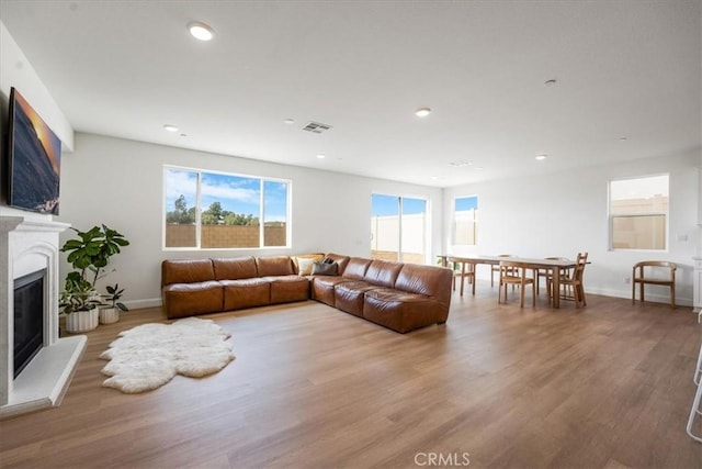 living room featuring wood finished floors, a glass covered fireplace, visible vents, and recessed lighting