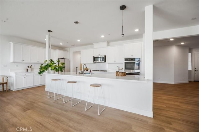 kitchen with appliances with stainless steel finishes, white cabinets, light wood-style floors, and hanging light fixtures