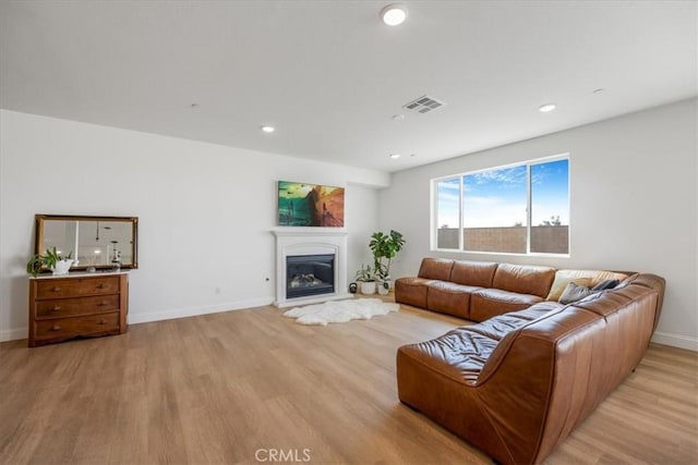 living area with light wood-style flooring, visible vents, baseboards, and a glass covered fireplace