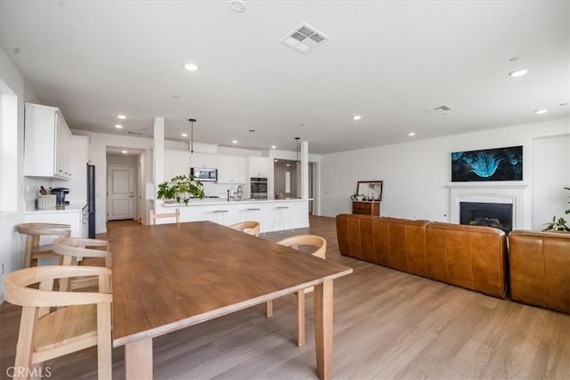 dining space with light wood-style floors, recessed lighting, visible vents, and a fireplace