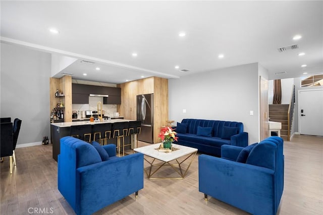 living room with recessed lighting, visible vents, light wood finished floors, and stairs