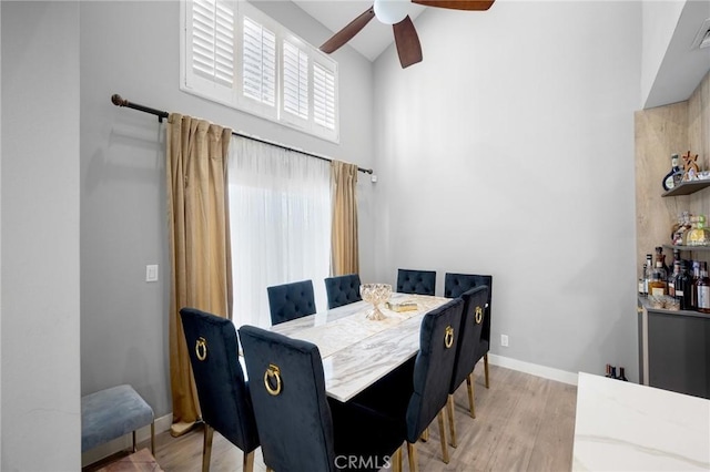 dining area with a ceiling fan, baseboards, high vaulted ceiling, and wood finished floors