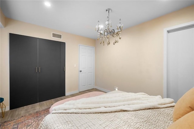 bedroom featuring a notable chandelier, a closet, visible vents, wood finished floors, and baseboards