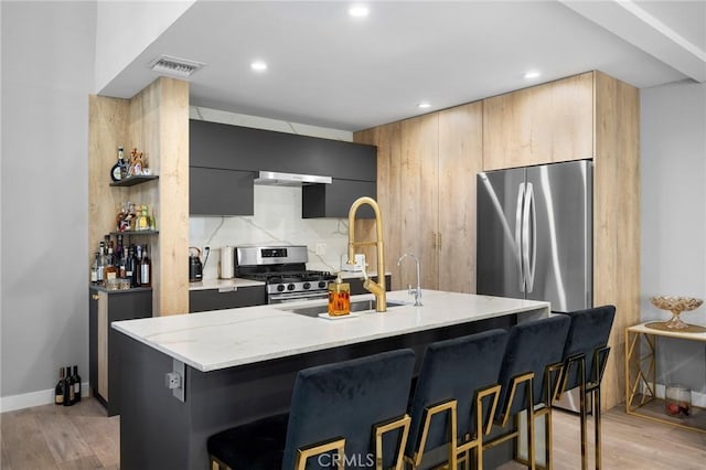 kitchen featuring visible vents, appliances with stainless steel finishes, modern cabinets, light wood-type flooring, and a kitchen bar