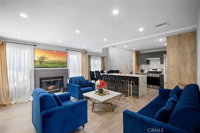 living room with light wood-type flooring, recessed lighting, visible vents, and a glass covered fireplace