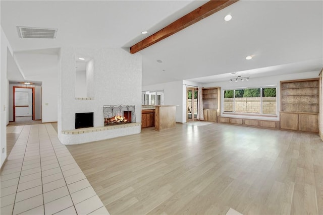 unfurnished living room with light wood-style flooring, visible vents, a fireplace, and lofted ceiling with beams