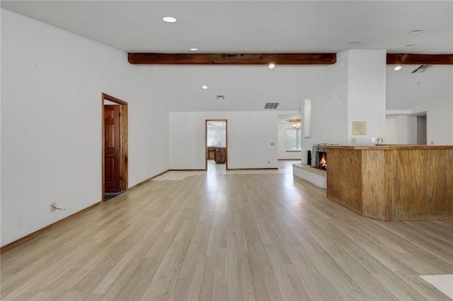 unfurnished living room featuring visible vents, baseboards, vaulted ceiling with beams, a lit fireplace, and light wood-style floors