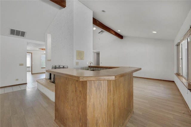 kitchen with light wood finished floors, baseboards, visible vents, and beam ceiling