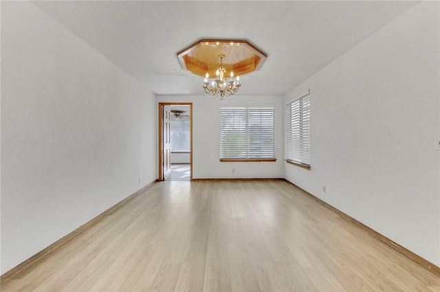 spare room with a chandelier, light wood-style flooring, and baseboards