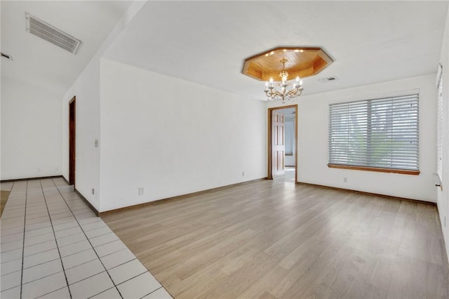 unfurnished room with light wood-type flooring, a raised ceiling, visible vents, and a notable chandelier