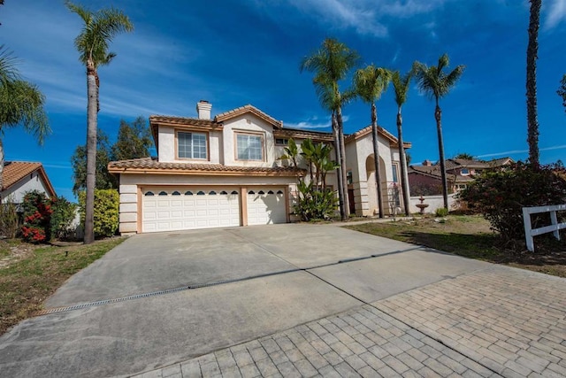 mediterranean / spanish house with a chimney, stucco siding, concrete driveway, an attached garage, and a tiled roof