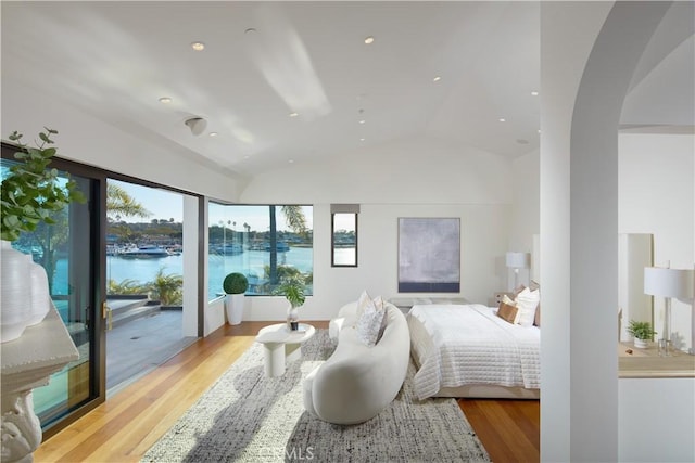 bedroom with arched walkways, lofted ceiling, access to outside, and light wood-type flooring