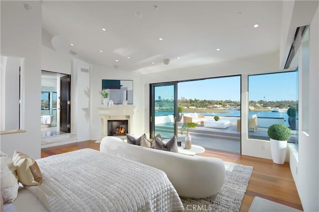 bedroom featuring access to outside, wood finished floors, recessed lighting, a glass covered fireplace, and vaulted ceiling