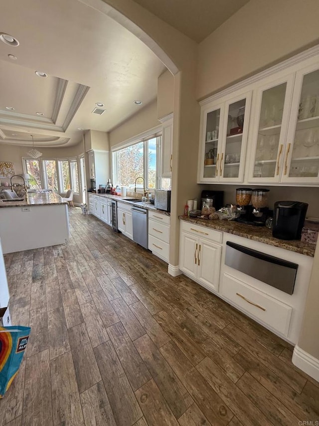 interior space featuring arched walkways, dark wood finished floors, a tray ceiling, stainless steel dishwasher, and a warming drawer