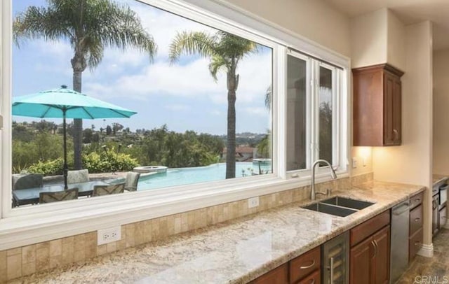 kitchen featuring wine cooler, brown cabinets, stainless steel dishwasher, a sink, and light stone countertops