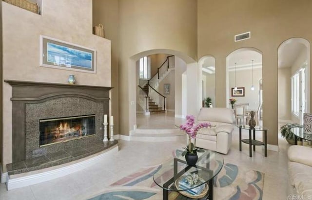 tiled living area featuring a fireplace, visible vents, a towering ceiling, baseboards, and stairs