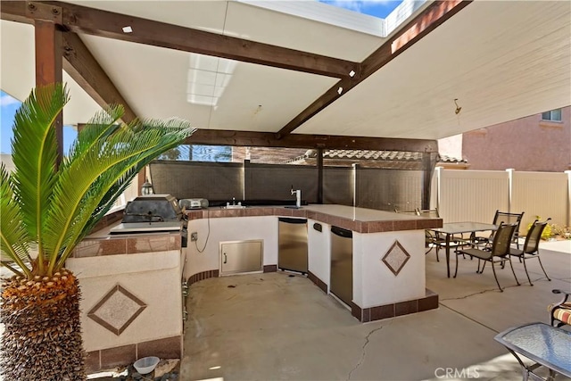 view of patio featuring area for grilling, fence, outdoor dining area, outdoor wet bar, and a sink