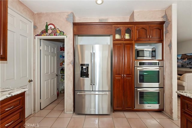 kitchen with light tile patterned floors, visible vents, appliances with stainless steel finishes, glass insert cabinets, and light stone countertops