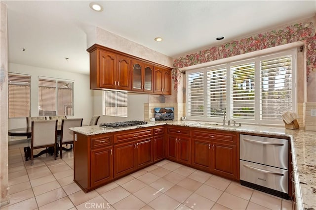 kitchen with brown cabinetry, a peninsula, light stone countertops, stainless steel gas stovetop, and a sink