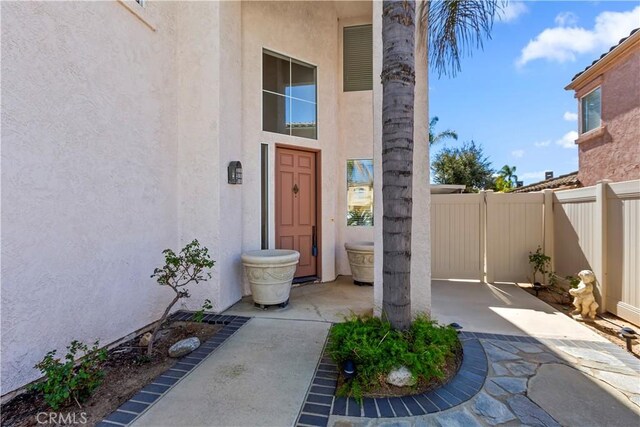 doorway to property with a patio area, fence, and stucco siding