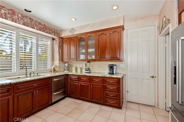 kitchen with decorative backsplash, glass insert cabinets, light tile patterned flooring, a sink, and light stone countertops