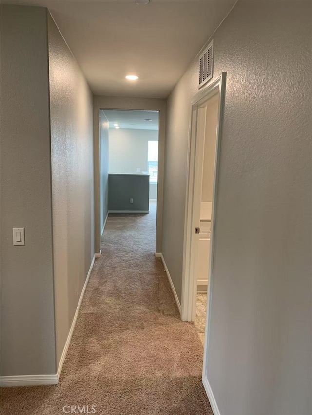 hallway featuring baseboards, visible vents, carpet flooring, and a textured wall