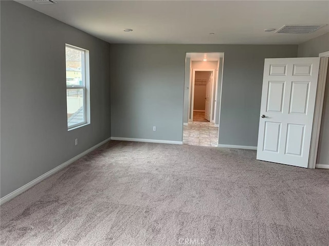 unfurnished bedroom with carpet floors, a walk in closet, visible vents, and baseboards