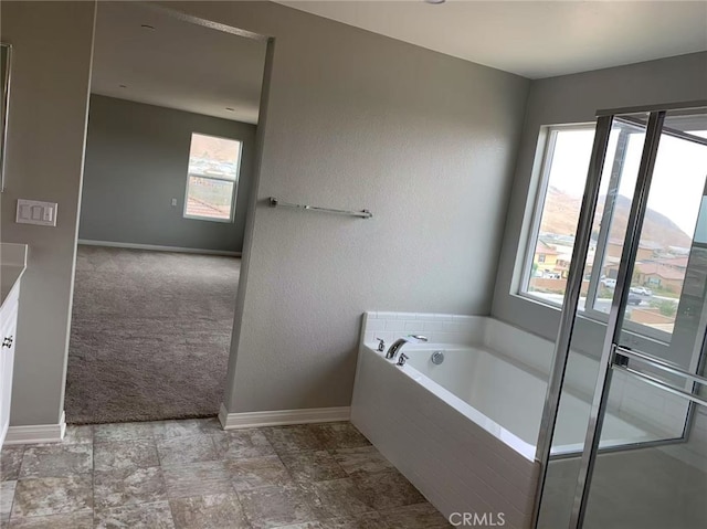 bathroom featuring baseboards, a garden tub, and a healthy amount of sunlight