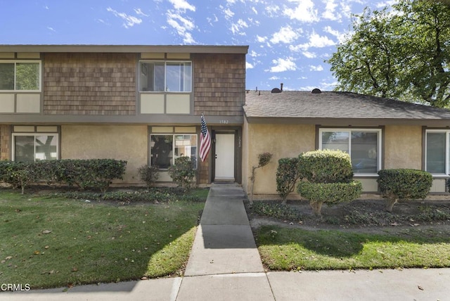 multi unit property with roof with shingles, a front lawn, and stucco siding