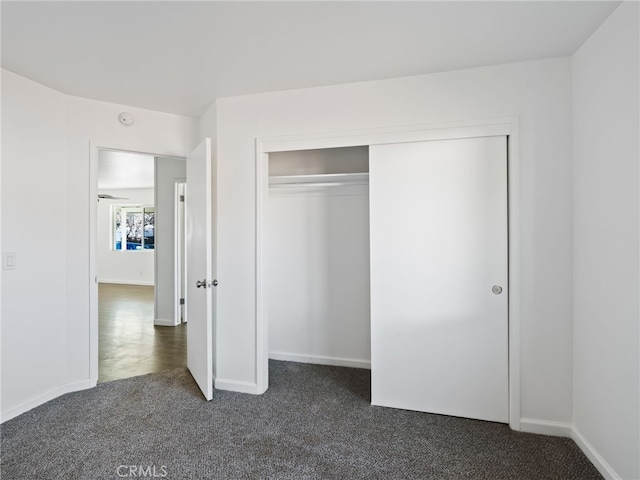 unfurnished bedroom featuring baseboards, dark colored carpet, and a closet