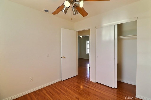 unfurnished bedroom with baseboards, visible vents, a ceiling fan, wood finished floors, and a closet