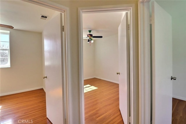 hall featuring visible vents, baseboards, and wood finished floors