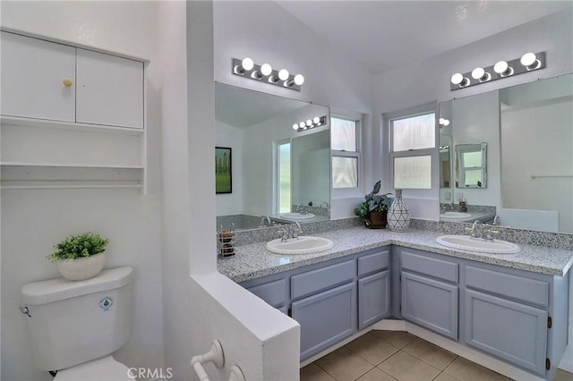 full bathroom with toilet, double vanity, a sink, and tile patterned floors