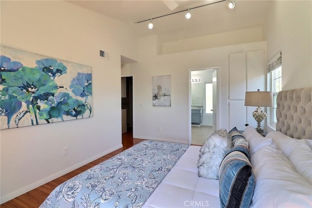 bedroom featuring baseboards, visible vents, ensuite bath, wood finished floors, and high vaulted ceiling