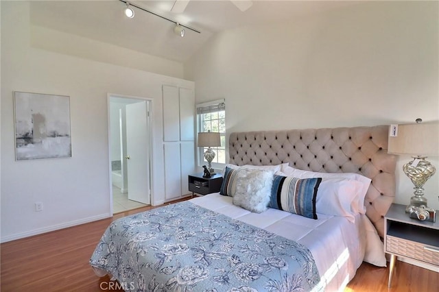 bedroom with connected bathroom, vaulted ceiling, track lighting, wood finished floors, and baseboards