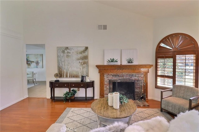 living area with visible vents, a brick fireplace, wood finished floors, high vaulted ceiling, and baseboards