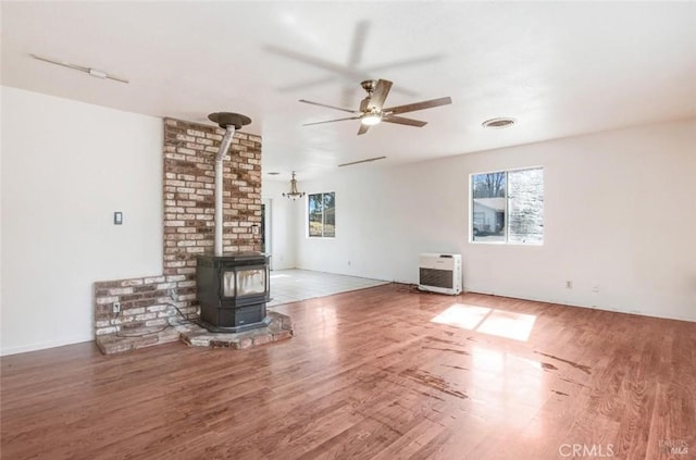 unfurnished living room with a wood stove, visible vents, plenty of natural light, and wood finished floors