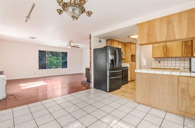 kitchen with light tile patterned floors, stainless steel fridge, tile countertops, open floor plan, and backsplash