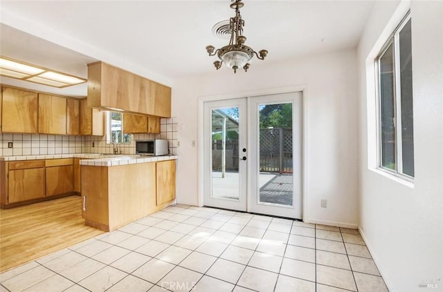 kitchen featuring light tile patterned floors, tasteful backsplash, tile counters, a peninsula, and french doors