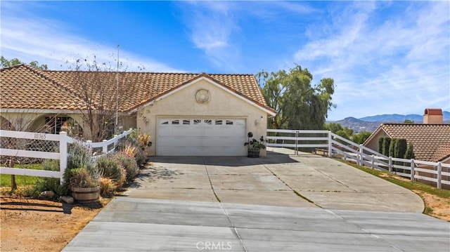 mediterranean / spanish home with stucco siding, a fenced front yard, a mountain view, concrete driveway, and a tiled roof