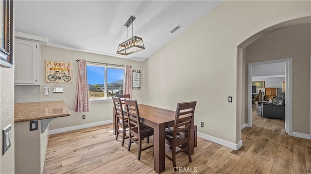 dining space featuring visible vents, arched walkways, light wood finished floors, and baseboards