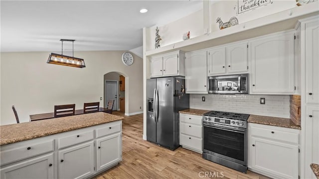 kitchen featuring tasteful backsplash, stainless steel appliances, arched walkways, light wood finished floors, and vaulted ceiling