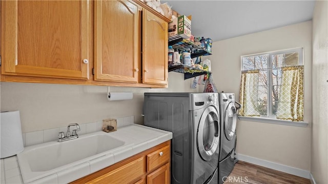 clothes washing area featuring a sink, washer and dryer, wood finished floors, cabinet space, and baseboards