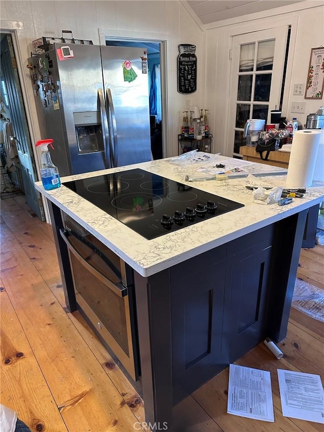 kitchen featuring a center island, stainless steel refrigerator with ice dispenser, black electric stovetop, light wood finished floors, and oven