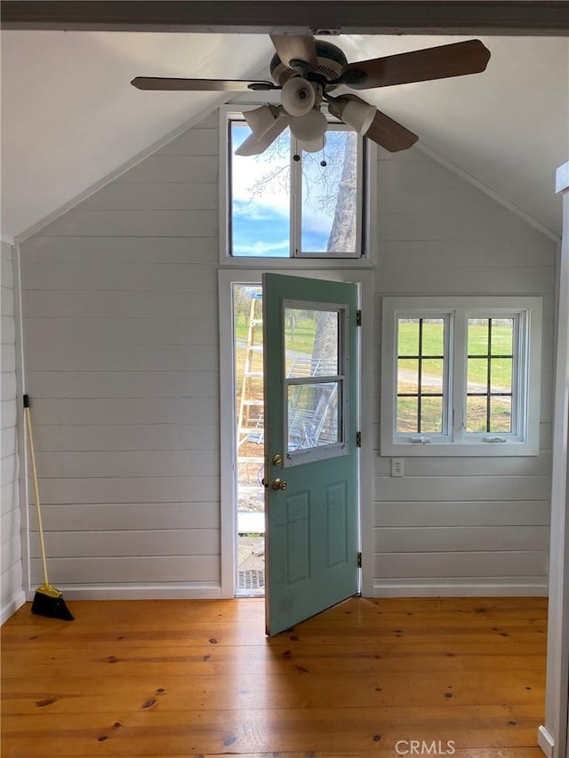 foyer featuring wood walls, vaulted ceiling, and light wood-style flooring