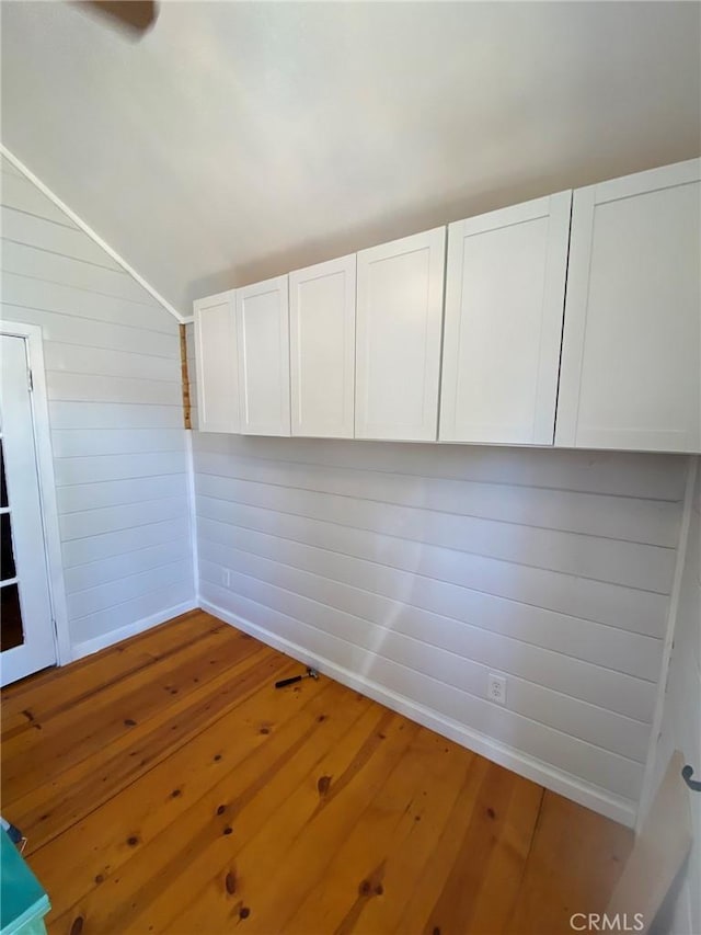 empty room featuring wood walls, vaulted ceiling, and hardwood / wood-style floors