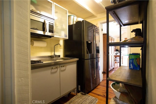 kitchen featuring glass insert cabinets, a sink, wood finished floors, dark countertops, and stainless steel appliances