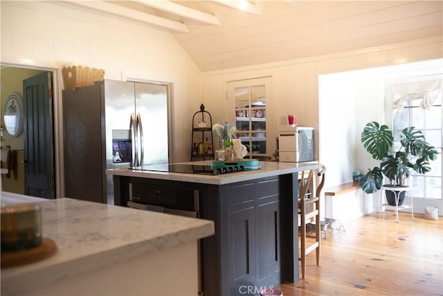 kitchen with lofted ceiling with beams, dark cabinets, stainless steel fridge, black electric stovetop, and light wood-style floors