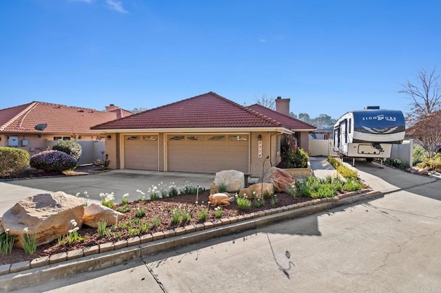 view of front of house with an attached garage, a tile roof, driveway, stucco siding, and a chimney