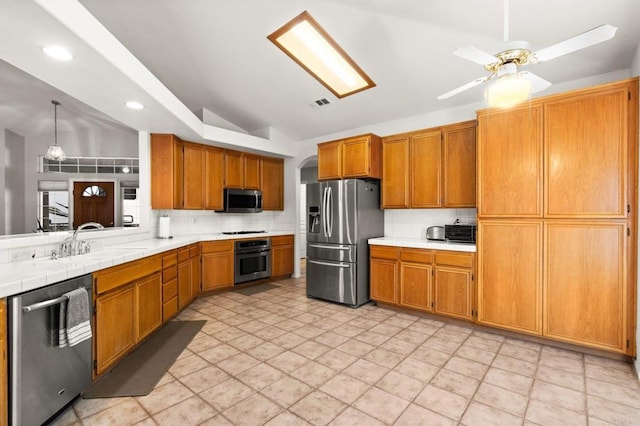 kitchen featuring appliances with stainless steel finishes, brown cabinets, a sink, vaulted ceiling, and backsplash